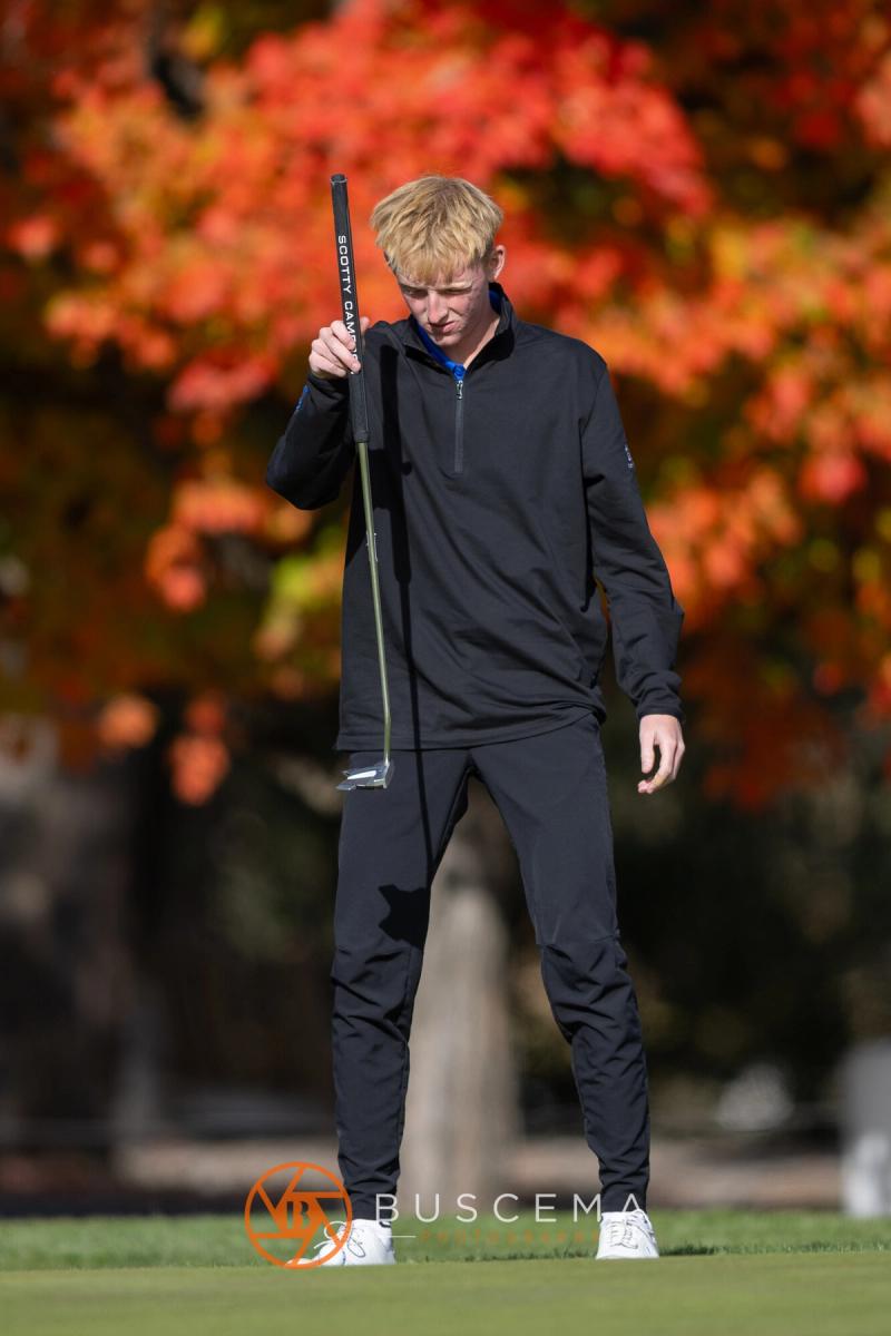 Golfer standing on the green in front of red fall leaves at the 6A state golf championships at Avondale Golf Club