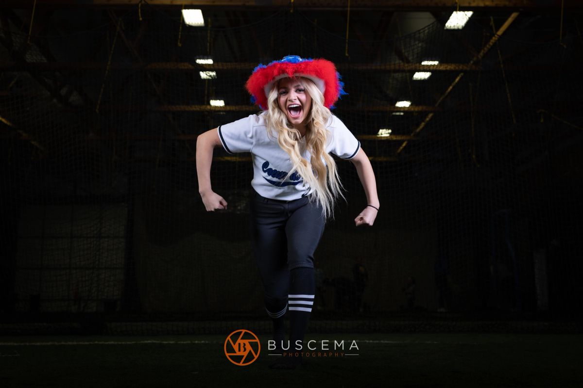 Energetic young woman jumping in indoor trampoline park wearing red and blue fuzzy hat and athletic outfit.