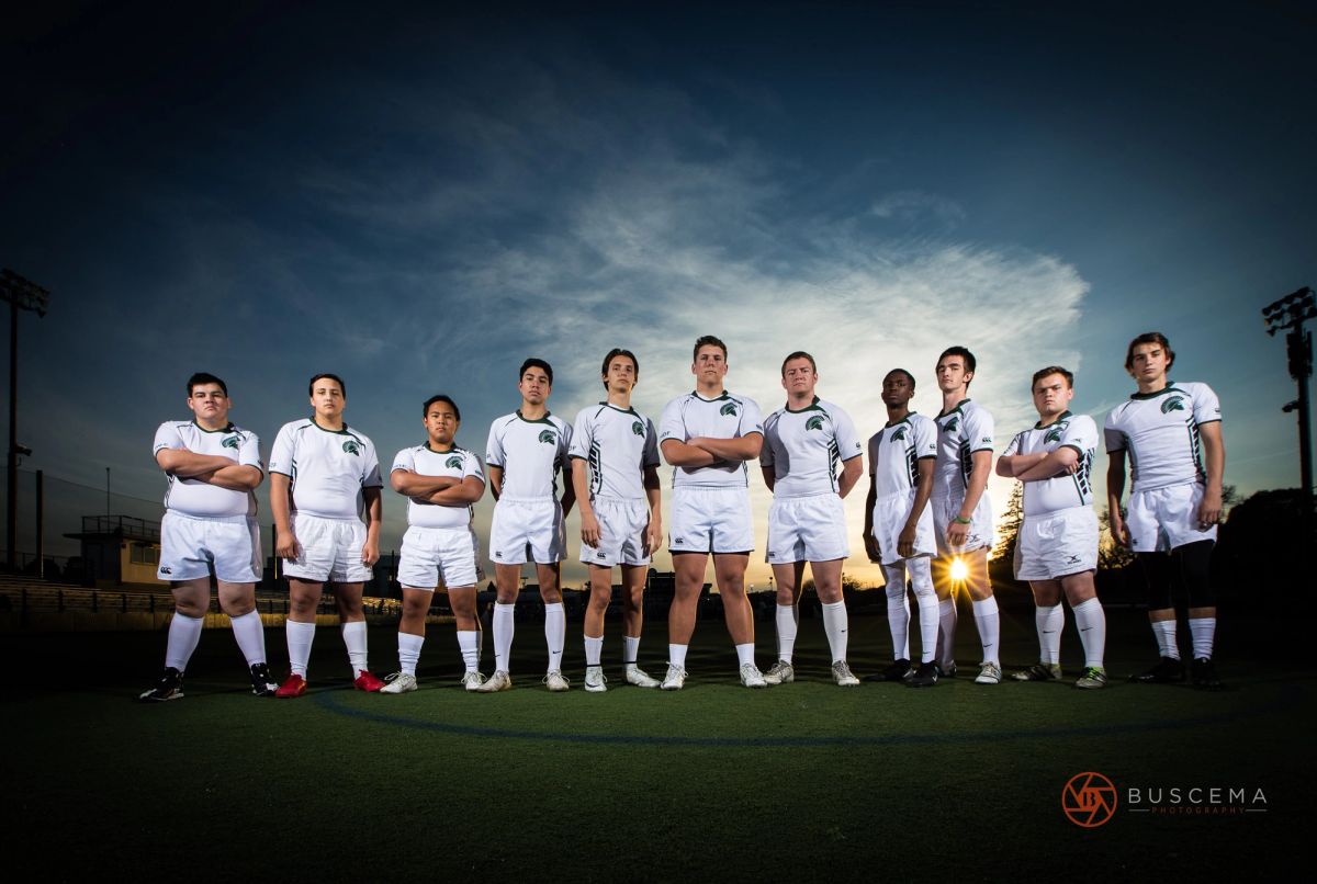 Soccer team in white uniforms lined up on field at sunset with stadium lights in background.
