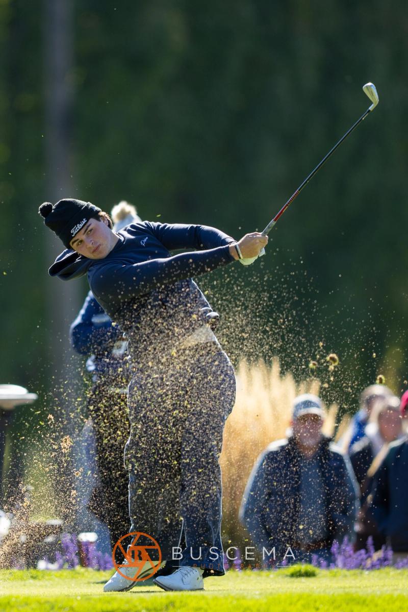 Golfer in a beanie hitting a tee shot with turf spraying at the 6A state golf championships at Avondale Golf Club