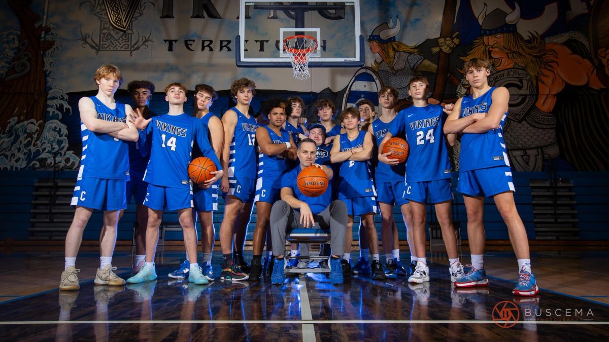 Vikings basketball team portrait with coach on gymnasium court, players in blue uniforms holding basketballs.