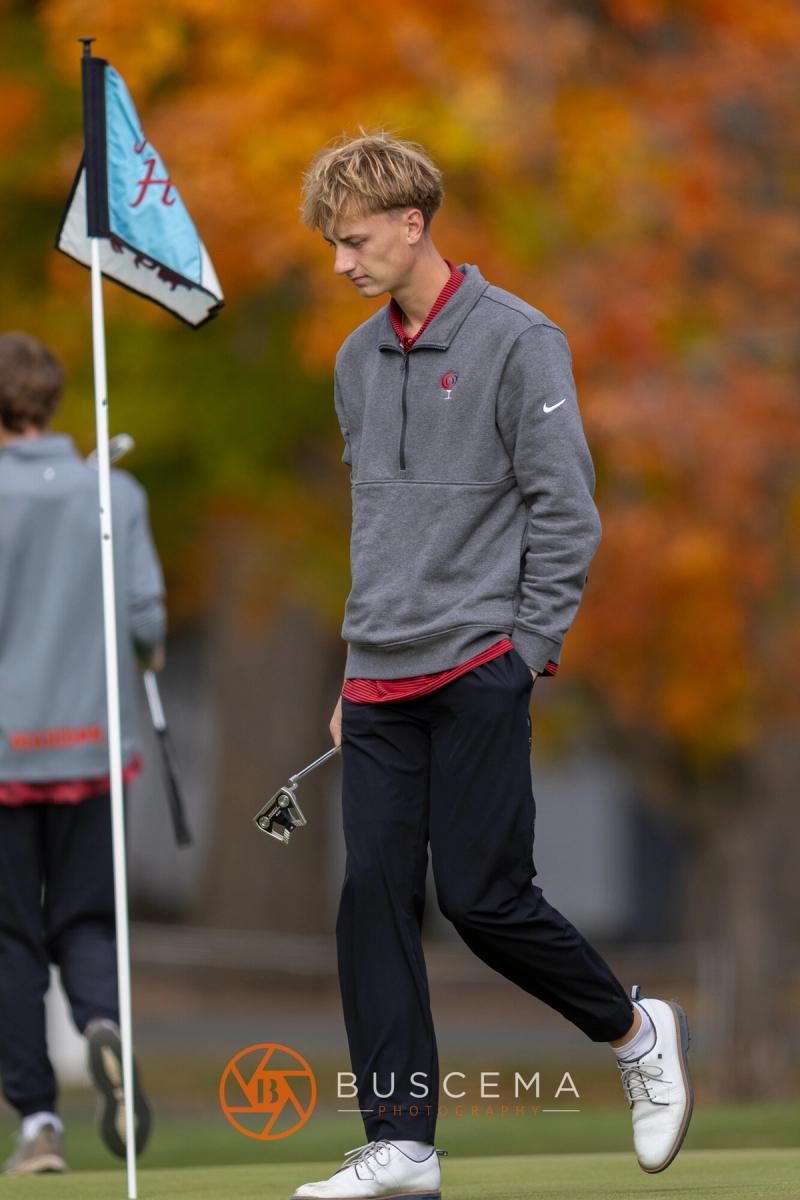 Boys golfer walking past the flag with fall leaves behind the green at the 6A state golf championships at Avondale Golf Club