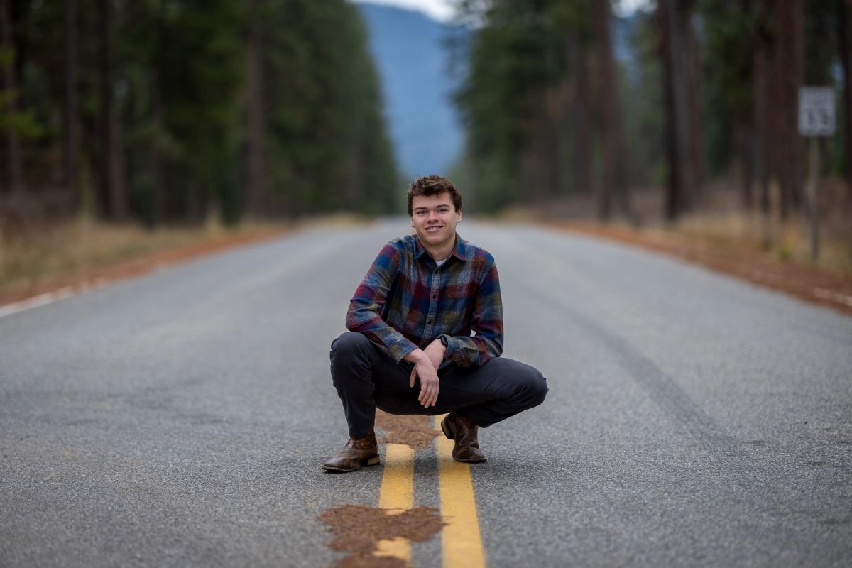 High school senior portrait of Ty Van Meeteren crouching on a forest road in North Idaho.