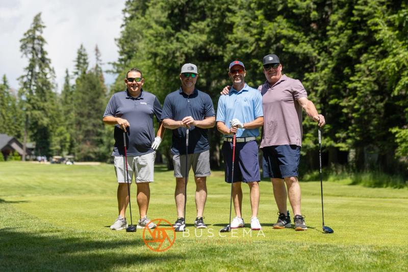 A foursome posing on the tee box surrounded by pine trees