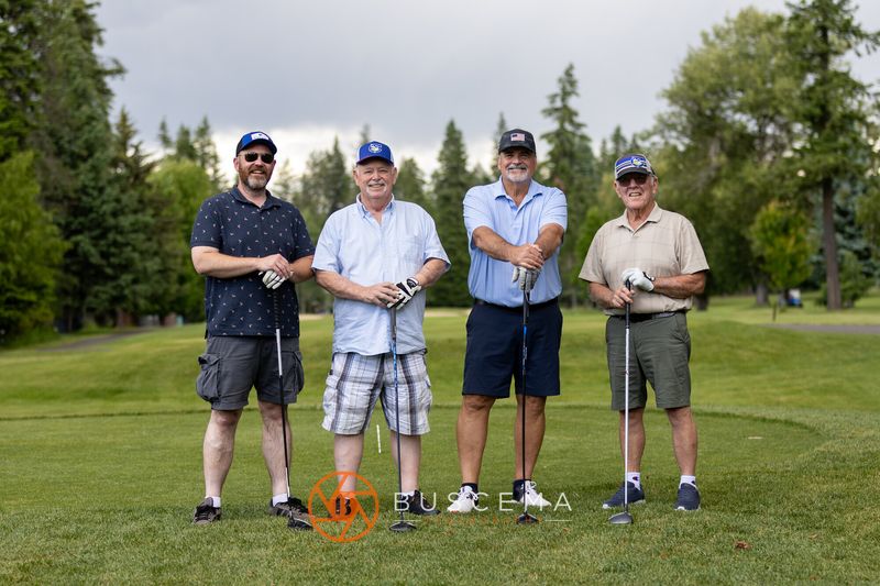 A foursome posing with their clubs under cloudy skies