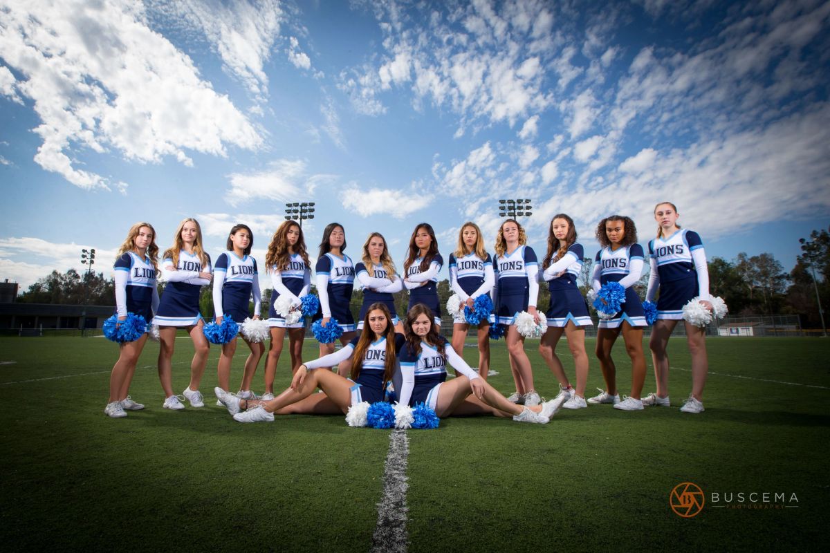 High school cheerleaders in blue and white Lions uniforms posing on a football field under stadium lights.