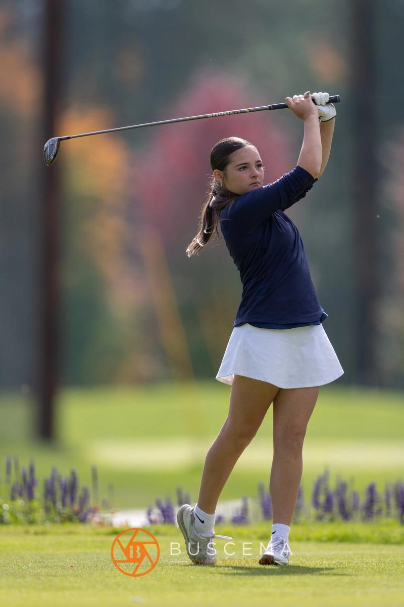 Girls golfer finishing her swing with fall colors behind her at the 6A state golf championships at Avondale Golf Club