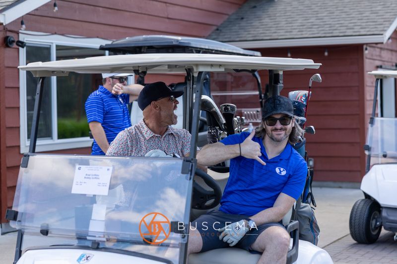 Two golfers in a cart flashing a hang loose sign