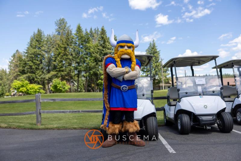 The Viking mascot posing with arms crossed next to golf carts on a sunny afternoon