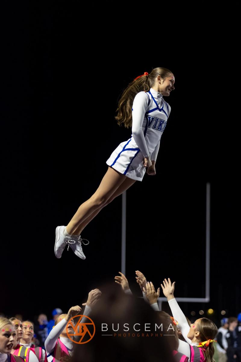 A Coeur d'Alene cheerleader at the top of a basket toss against the night sky