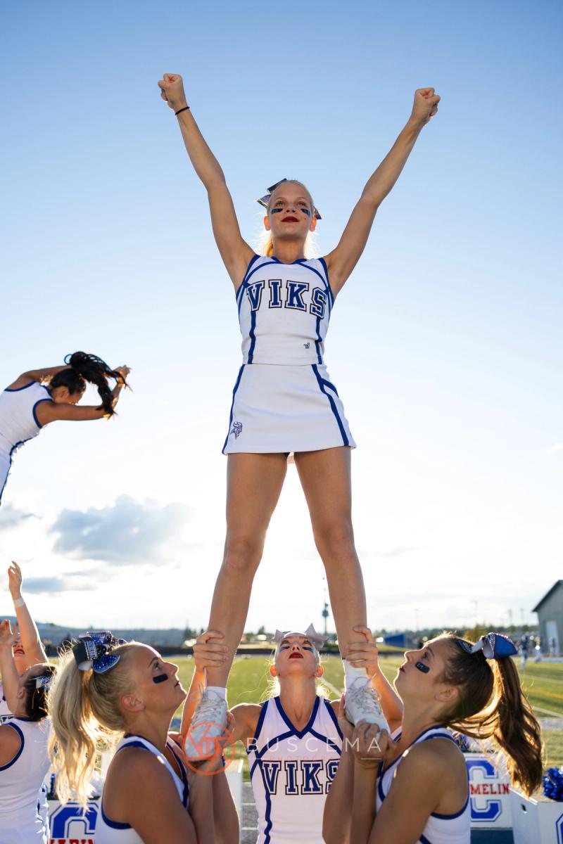 Coeur d'Alene cheer flyer held up in a stunt with her arms raised against a blue sky