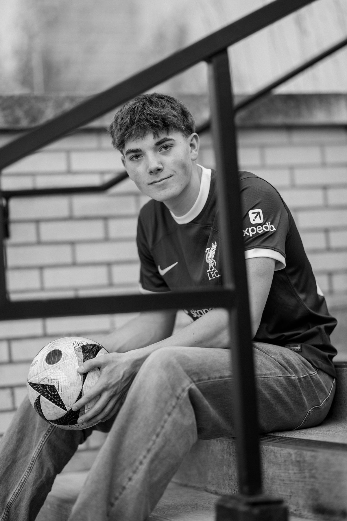 Black and white senior portrait of a Coeur d'Alene soccer player seated on steps holding a ball
