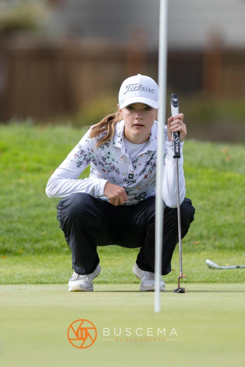 Girls golfer crouched behind the flagstick reading her putt at the 6A state golf championships at Avondale Golf Club