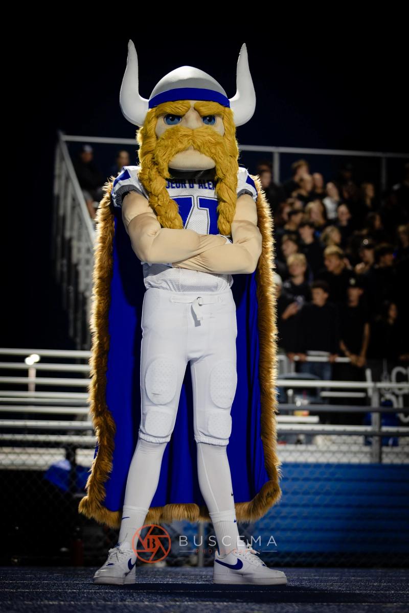 The Coeur d'Alene Viking mascot standing with arms crossed in front of the student section at night