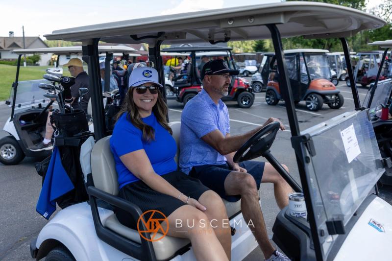 A golfer and his partner in a CHS hat smiling from their cart