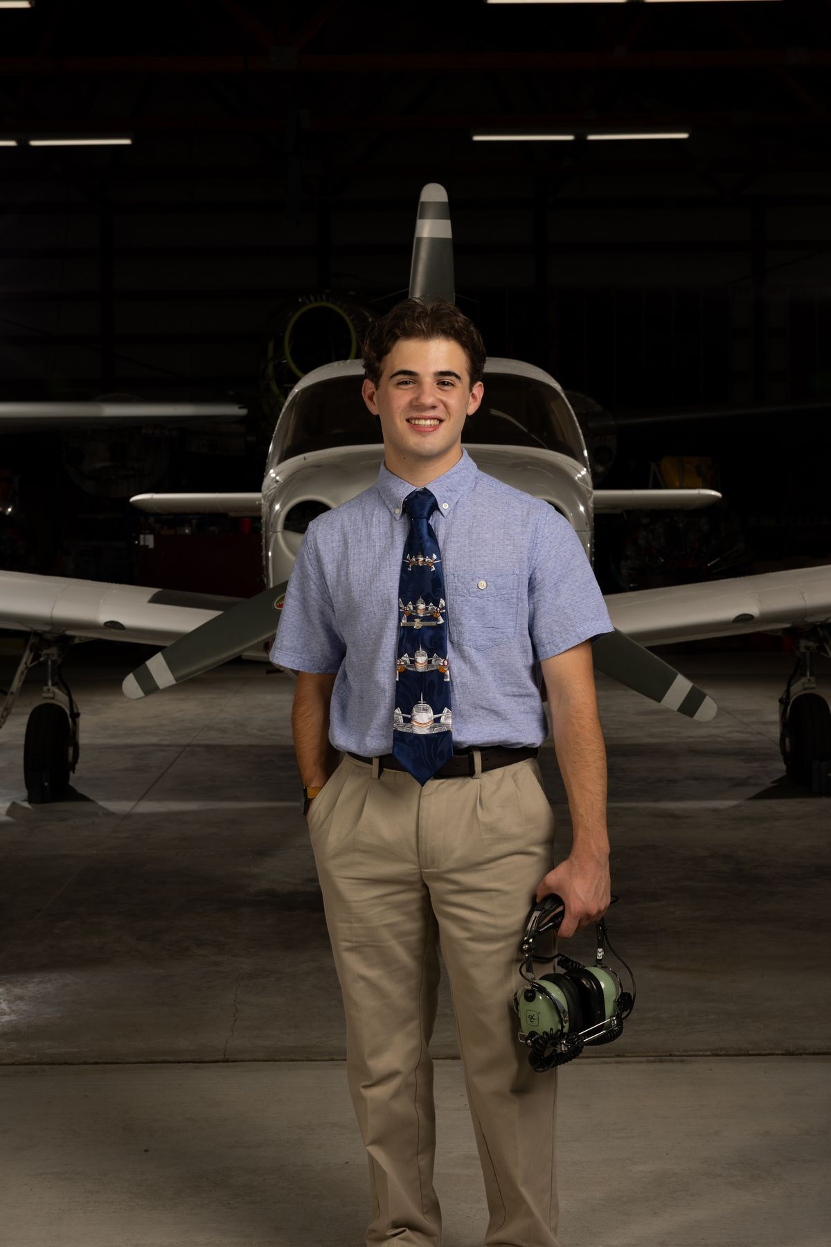Coeur d'Alene high school senior in a shirt and tie holding a headset in front of a small airplane