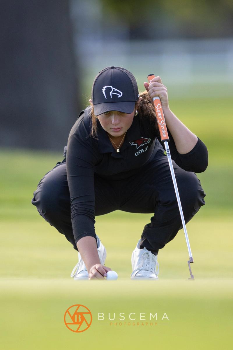 Girls golfer crouched behind her ball reading the putt at the 6A state golf championships at Avondale Golf Club