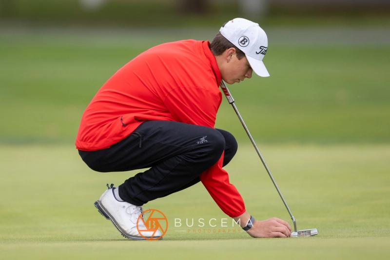 Golfer in a red jacket crouched to mark his ball at the 6A state golf championships at Avondale Golf Club