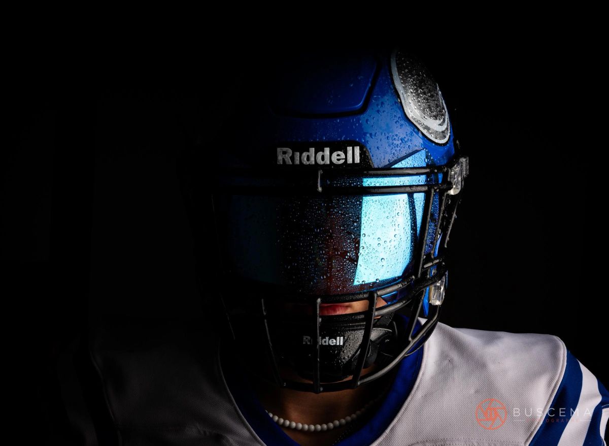 Close-up of a blue Riddell football helmet with face mask against a black background, water droplets visible on the surface.