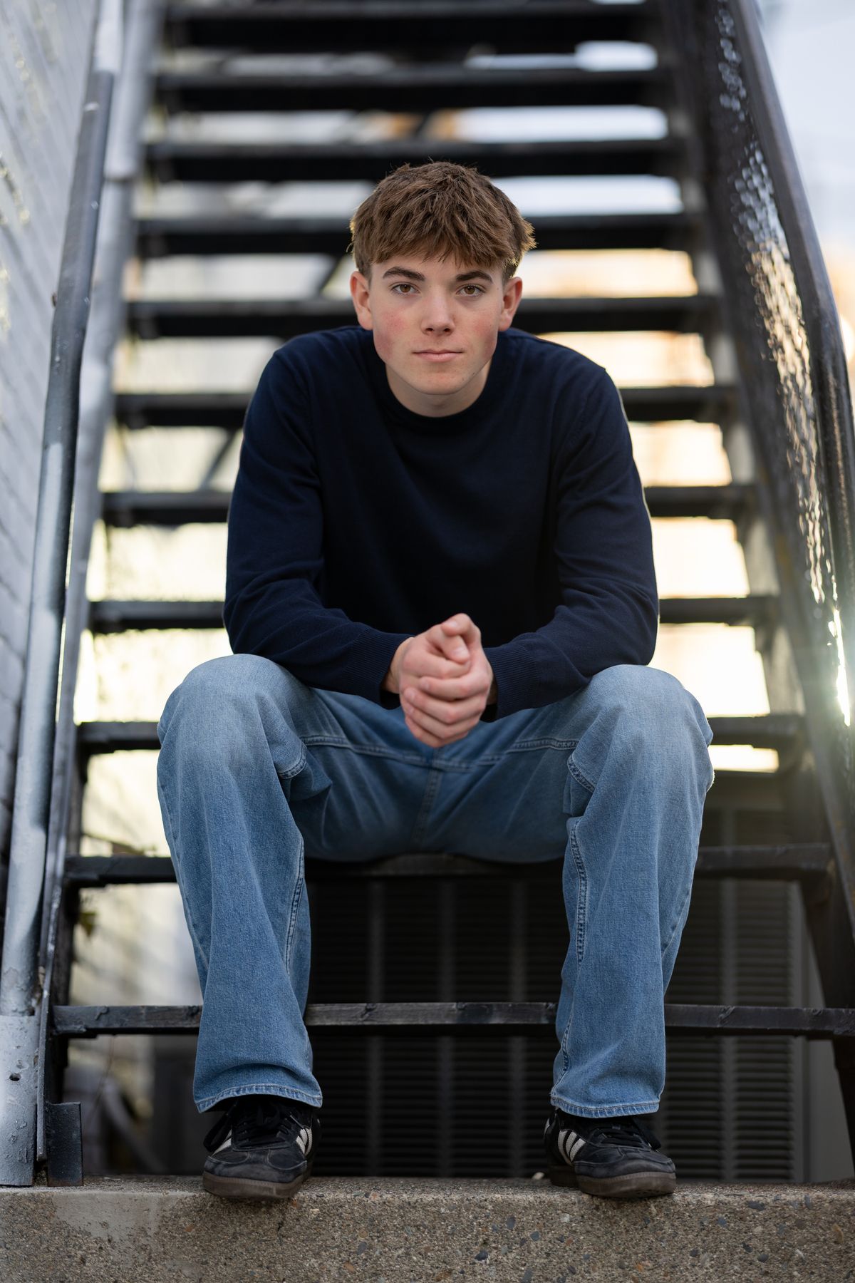 Coeur d'Alene high school senior in a navy sweater seated on a metal staircase