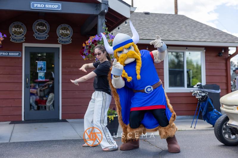 A golfer striking a pose with the Viking mascot in front of the pro shop