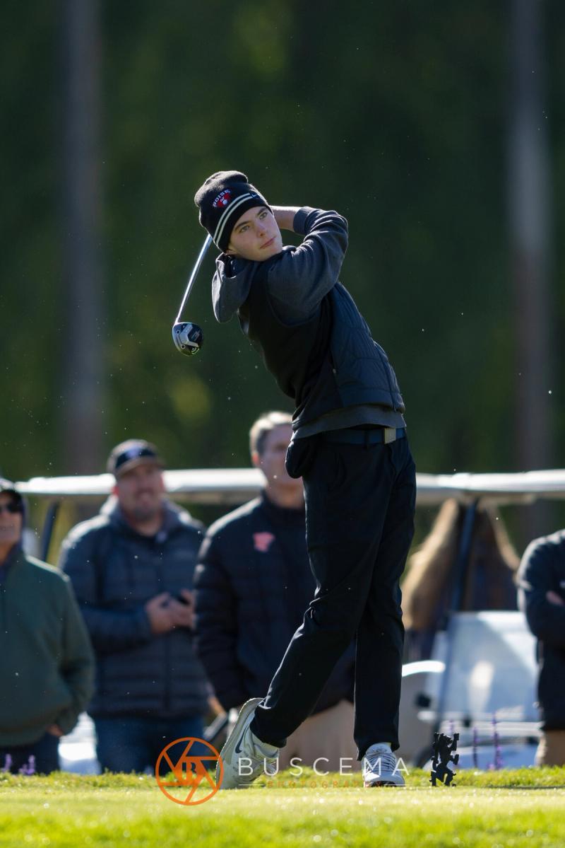 Boys golfer following through on a tee shot as spectators watch at the 6A state golf championships at Avondale Golf Club