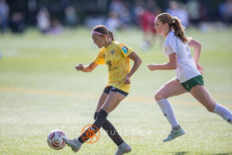 Sting 13G Academy player kicking the ball upfield ahead of a Harbor Premier defender