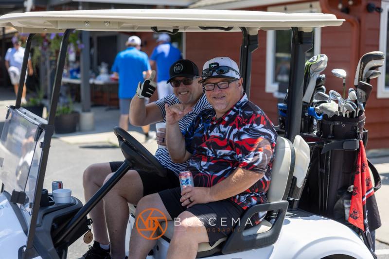 Two golfers in a cart waving on their way to the course