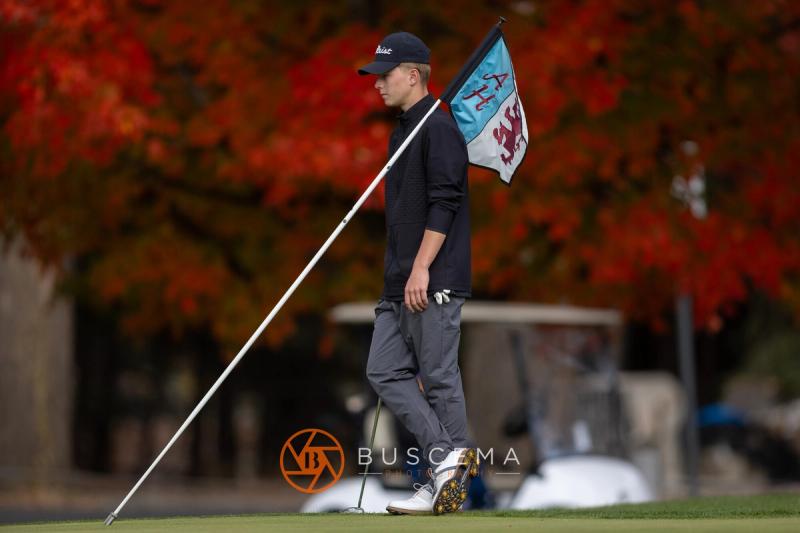 Golfer holding the flagstick in front of a bright red maple at the 6A state golf championships at Avondale Golf Club