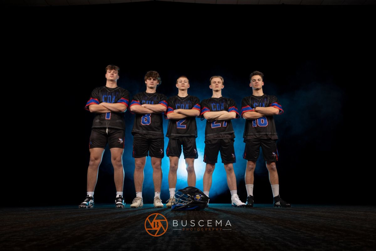 Five male lacrosse players in black and blue CHS uniforms stand with arms crossed against a dark background, with a helmet at their feet.