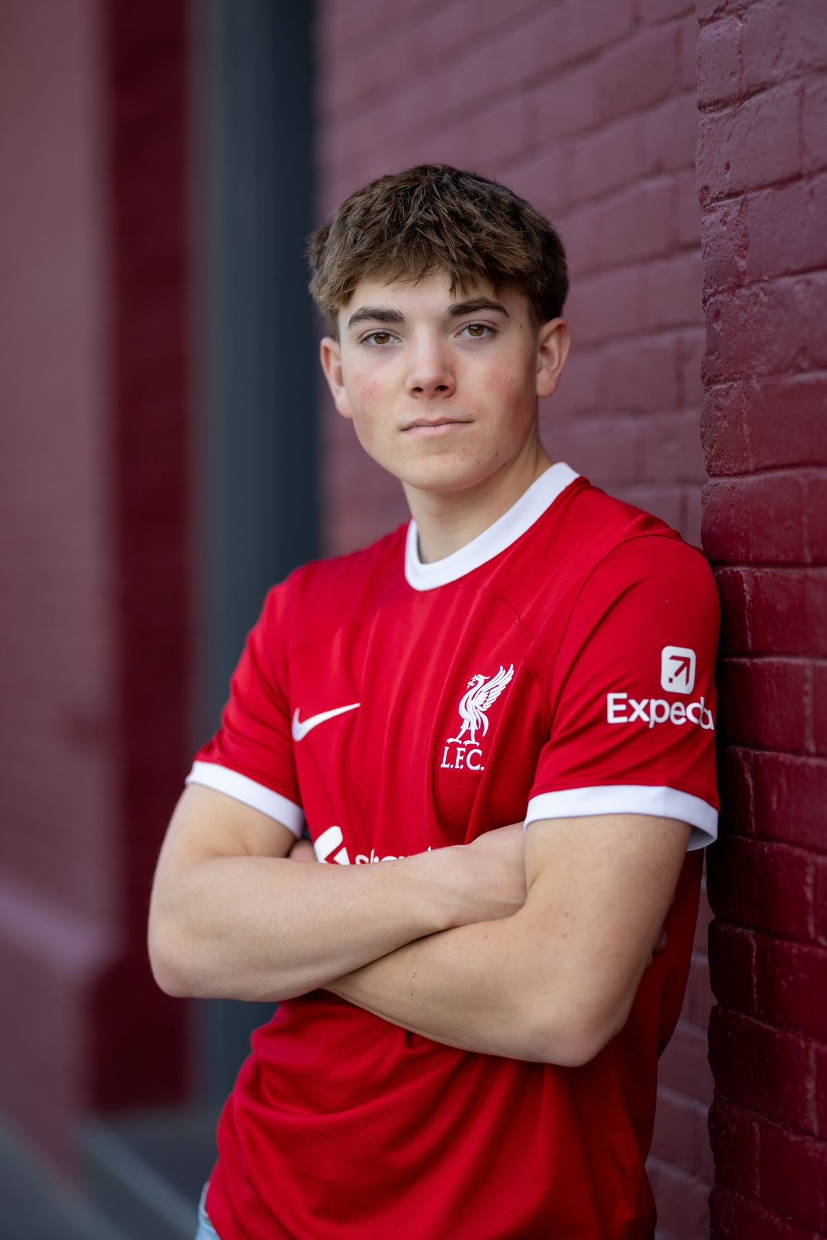 Coeur d'Alene senior soccer player in a red kit with arms crossed against a red brick wall