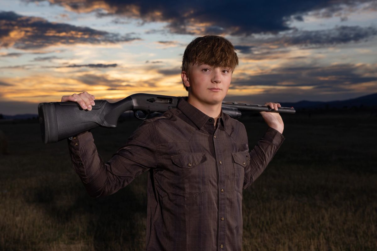 Young man holding rifle over shoulder at sunset in outdoor landscape setting.