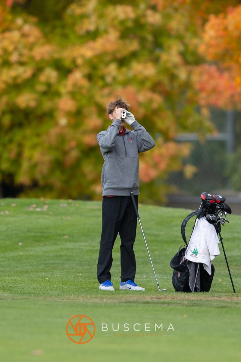 Golfer checking the yardage with a rangefinder under autumn trees at the 6A state golf championships at Avondale Golf Club