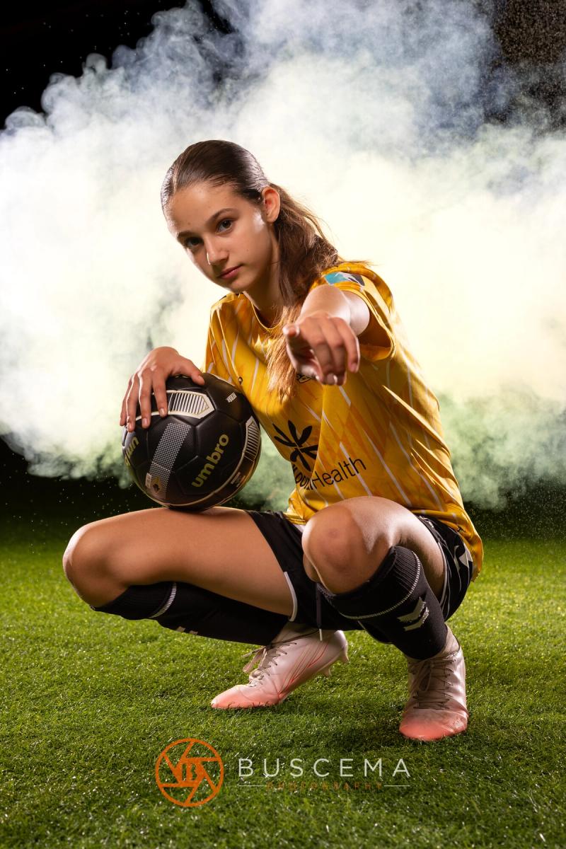Sting 13G Academy player crouched with a ball, pointing in the smoke