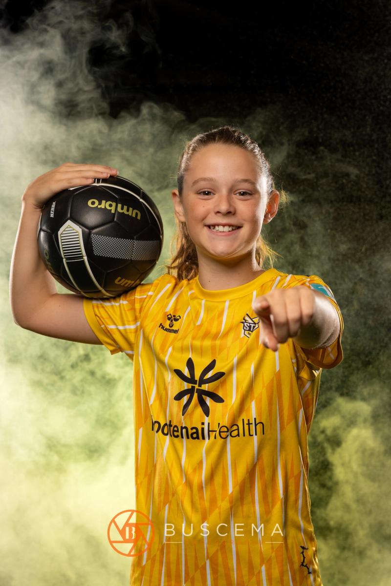 Smiling Sting 13G Academy player pointing with a ball on her shoulder