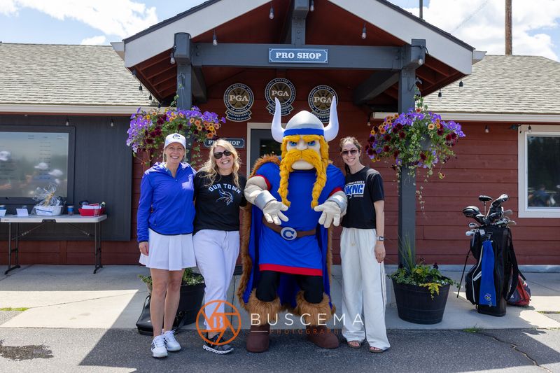 Three women posing with the Viking mascot in front of the Avondale pro shop