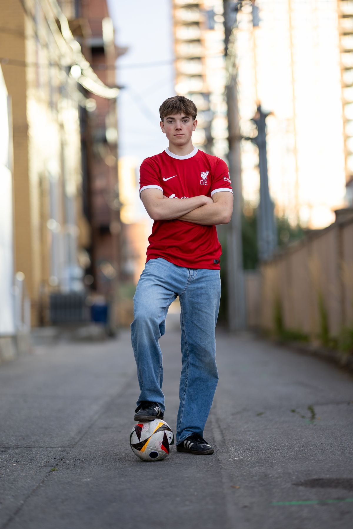 Coeur d'Alene senior soccer player standing in a downtown alley at golden hour with a ball at his foot