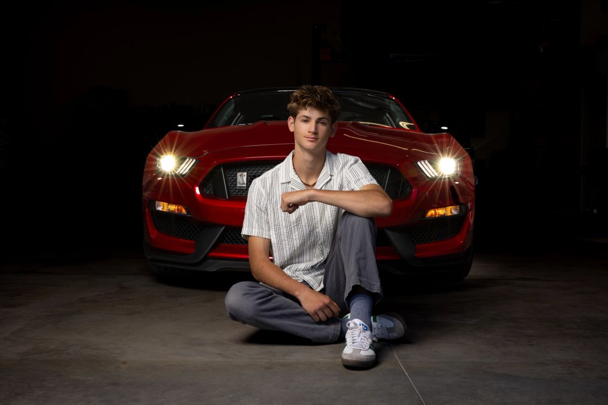 Coeur d'Alene high school senior seated in front of a red Mustang with the headlights on at night