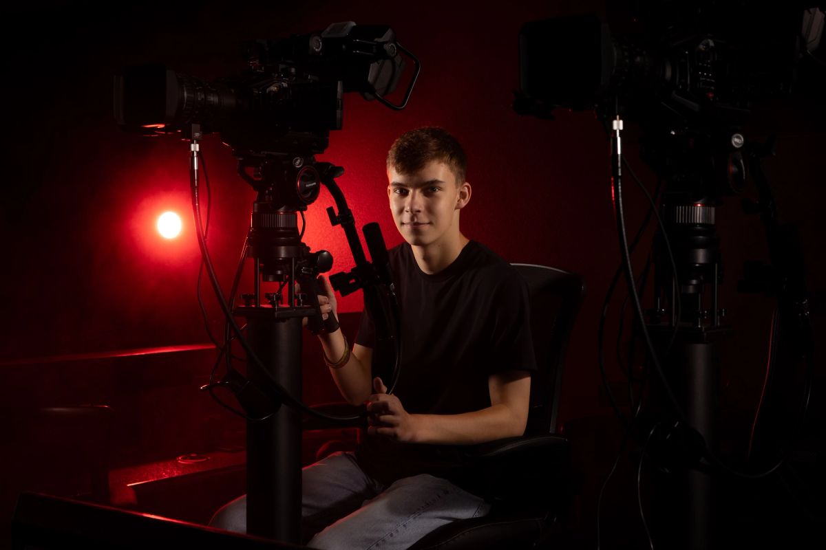 Young man operating professional camera equipment in red-lit studio setup, portrait photography session.