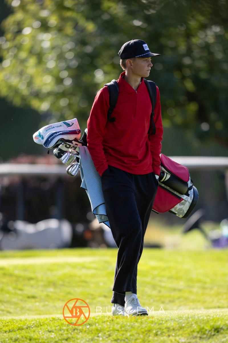 Golfer in a red jacket walking off the tee carrying his bag at the 6A state golf championships at Avondale Golf Club