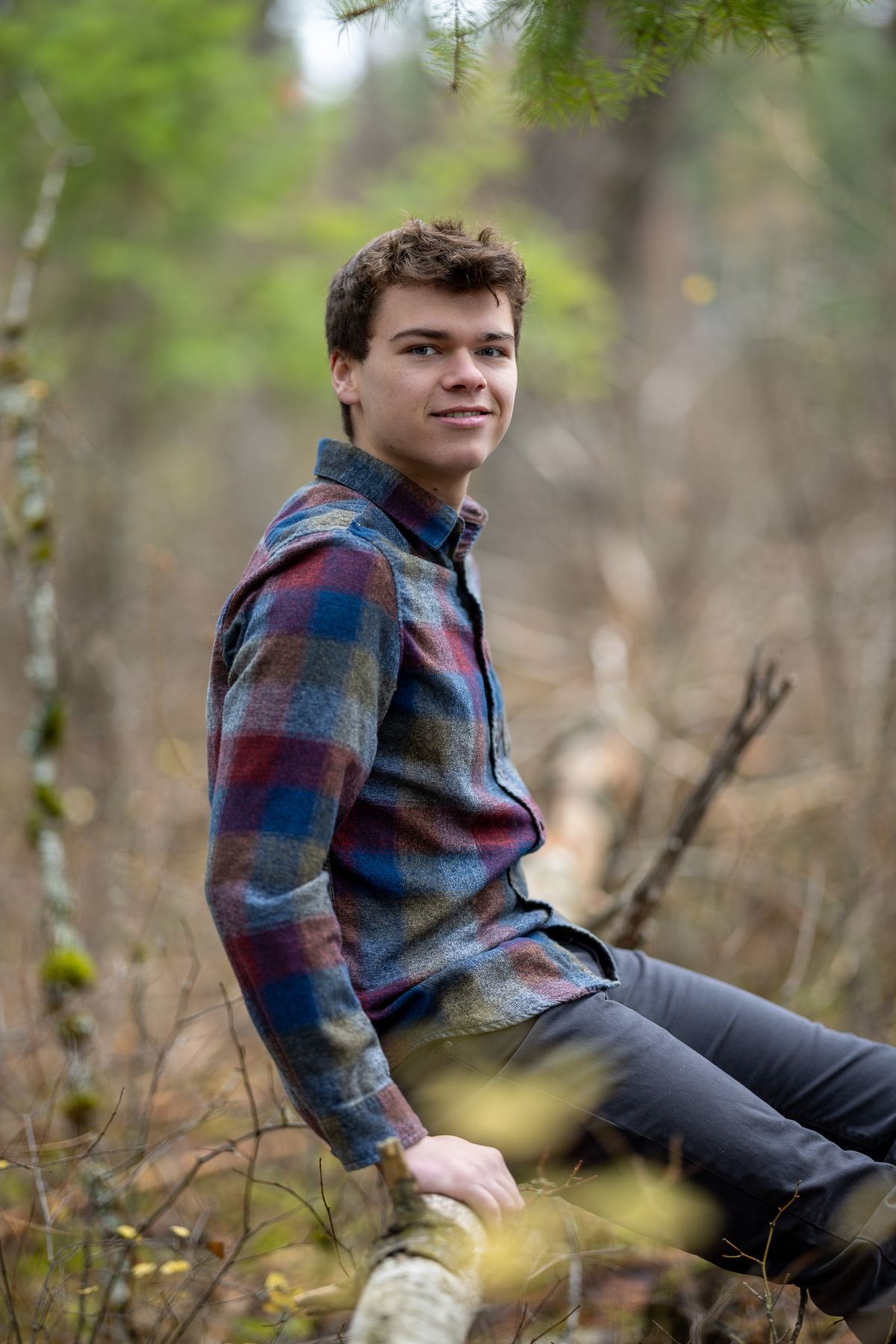 Portrait of Ty Van Meeteren, a high school senior, posing outdoors in a forest setting wearing a plaid shirt.