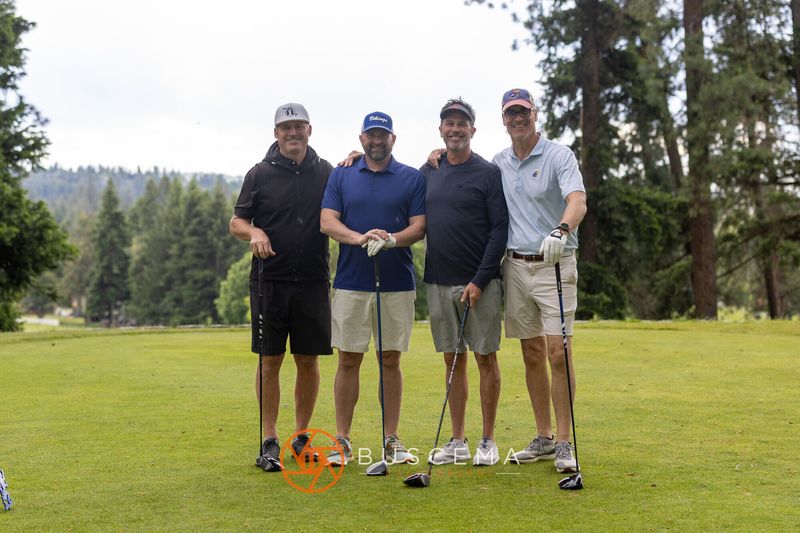 A foursome posing on the tee box with pine trees behind them