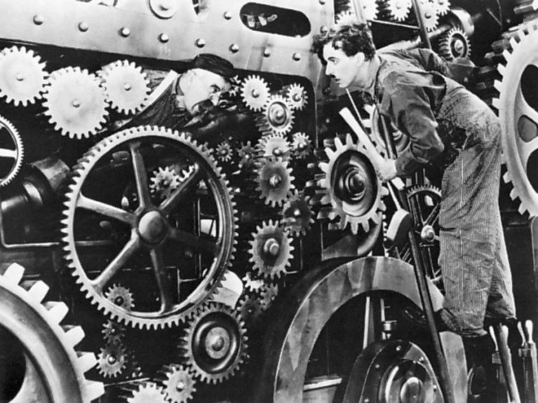 Still from Modern Times. Charlie Chaplin’s character inspects the giant gears of the factory machines.