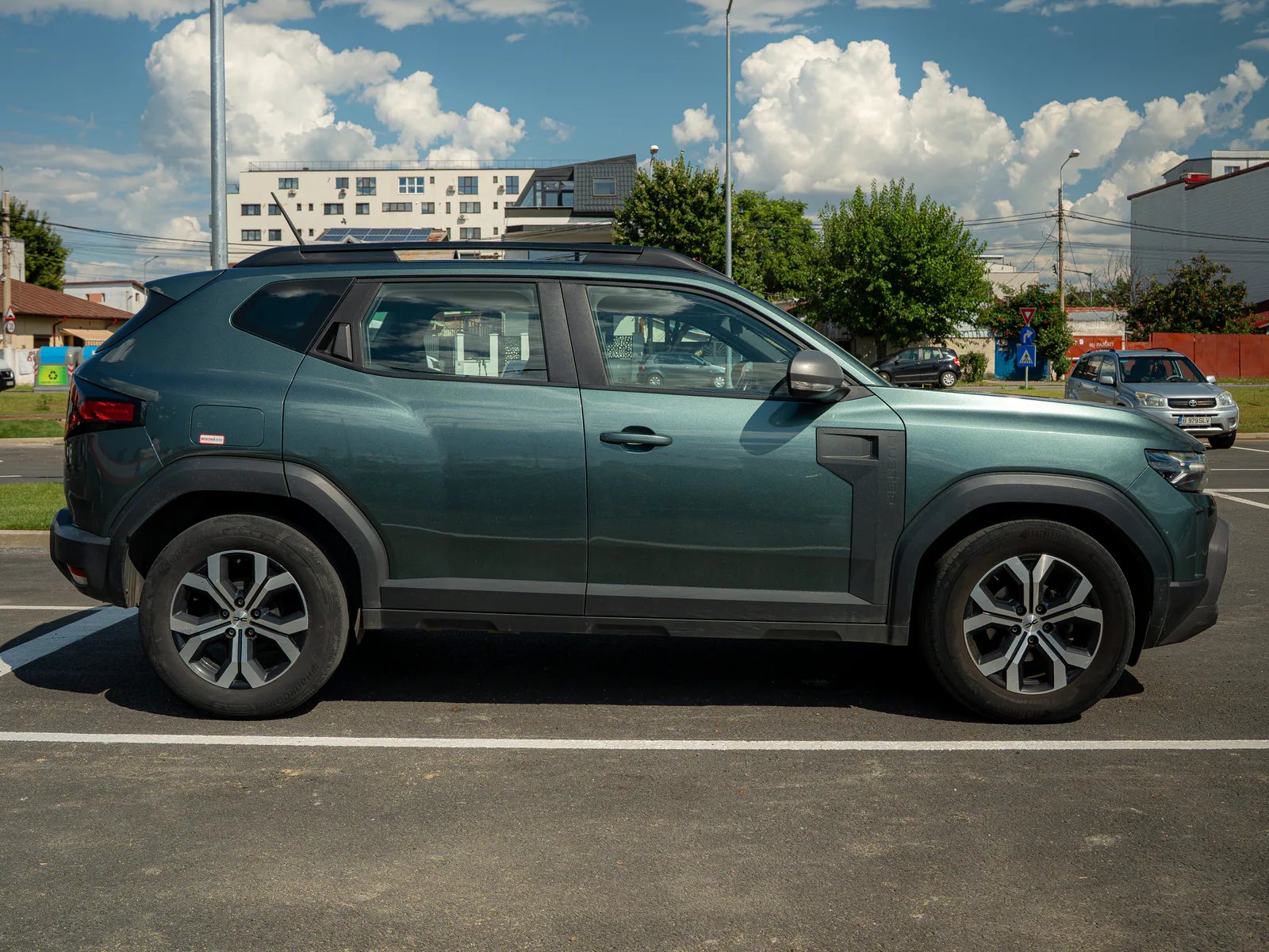 Profil lateral al unei Dacia Duster verde, fotografiată într-o parcare din București