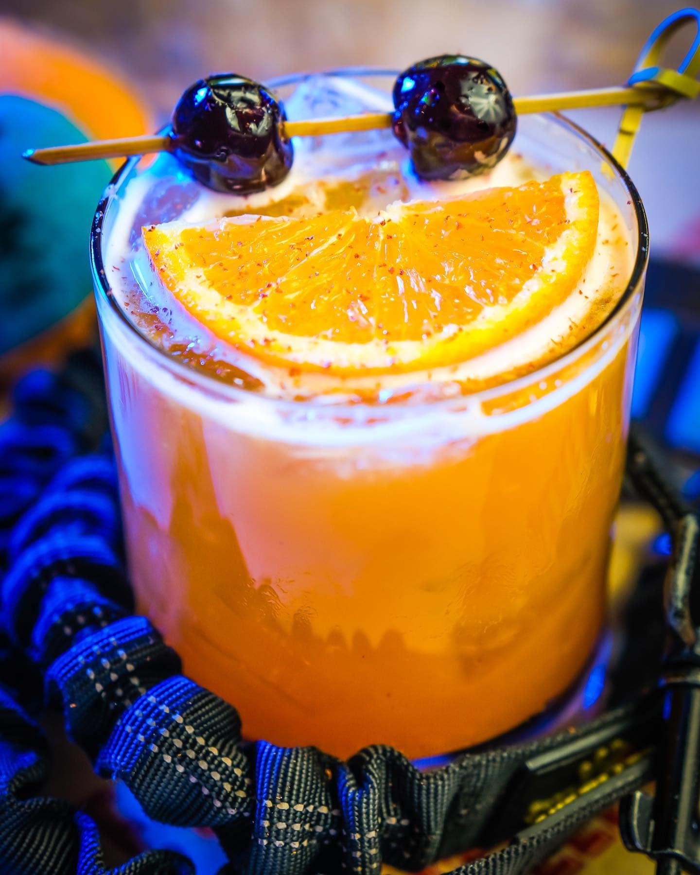 A bright orange cocktail in a lowball glass, garnished with an orange wedge and two maraschino cherries on a skewer