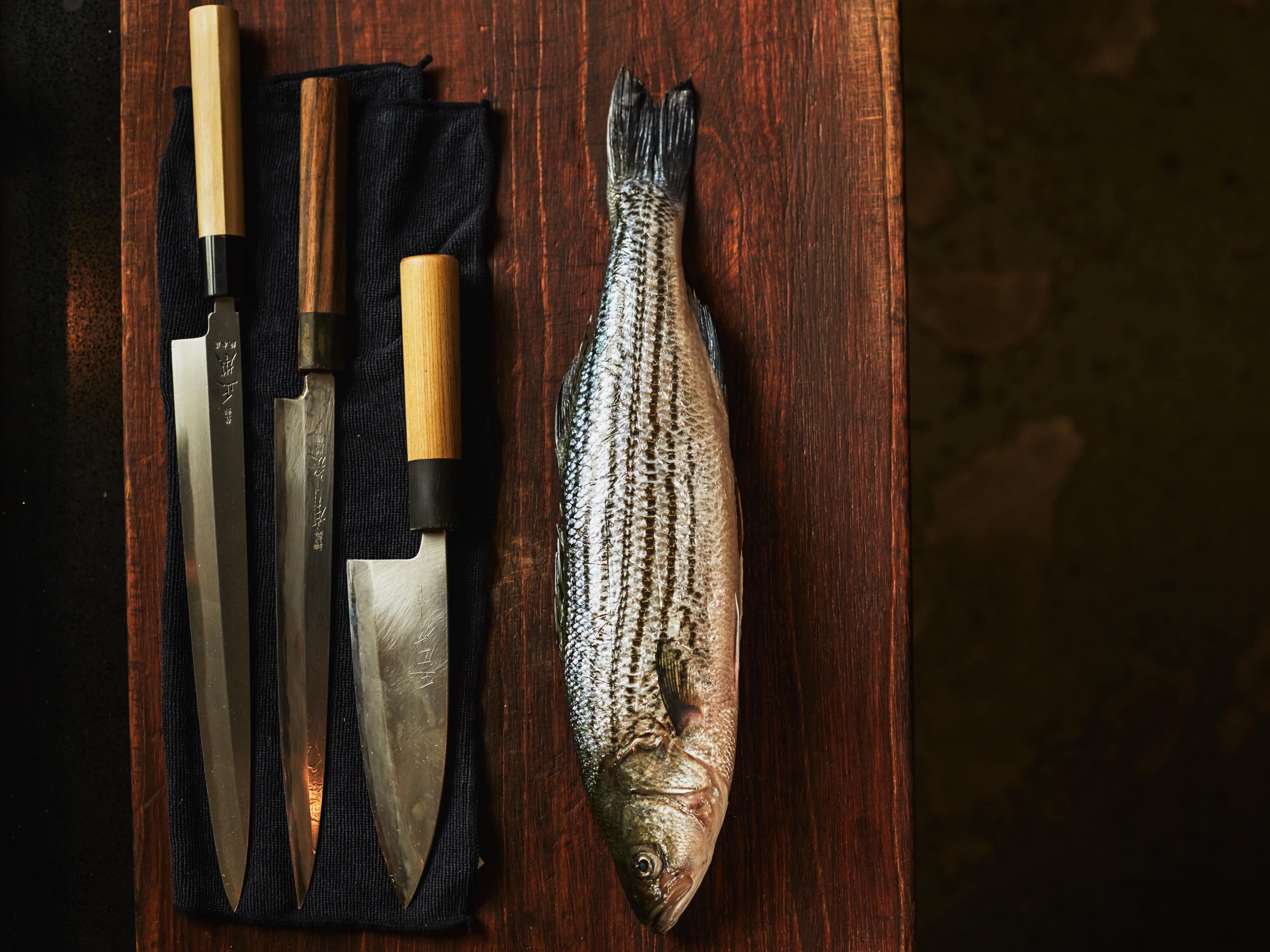 A whole fish on a cutting board next to a few chef knives at a Bamboo Sushi location. 