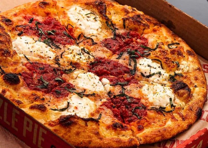 A delicious-looking pizza with ricotta and basil, nestled inside of a red pizza box