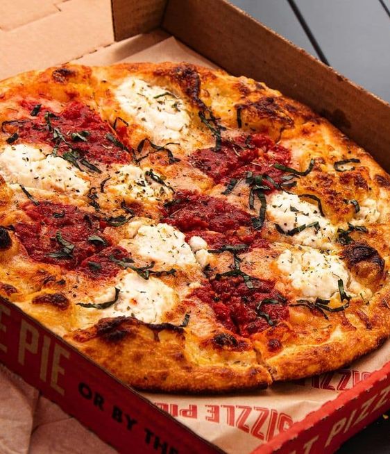 A delicious-looking pizza with ricotta and basil, nestled inside of a red pizza box