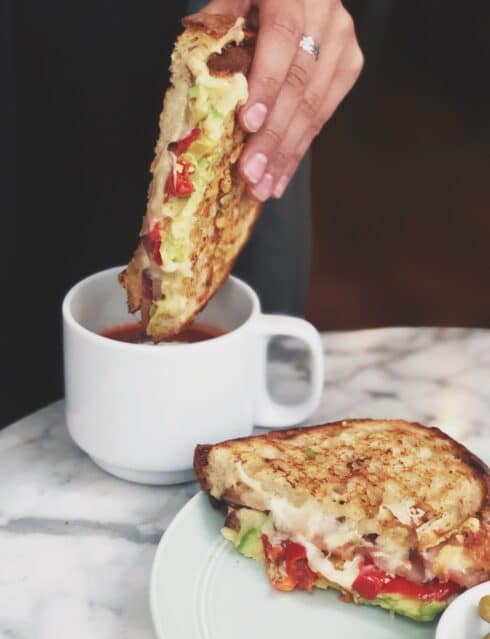 A toasty, melty sandwich being dipped into a cup of soup
