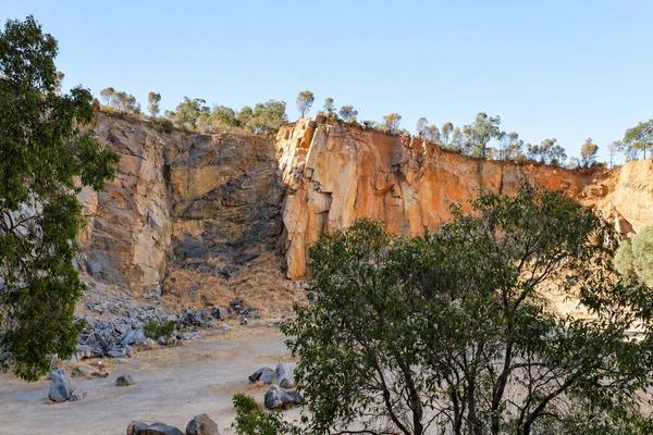 A tall orange and grey quarry wall in late afternoon light, framed by gum trees.